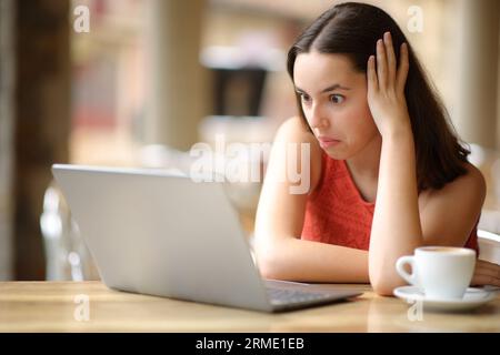 Verblüffte Frau, die auf einer Bar-Terrasse auf absurde Inhalte von Laptops schaut Stockfoto