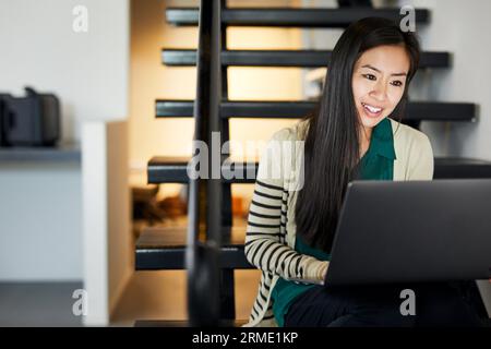Lächelnde, selbstbewusste Geschäftsfrau, die einen Laptop benutzt, während sie im Büro auf Stufen sitzt Stockfoto