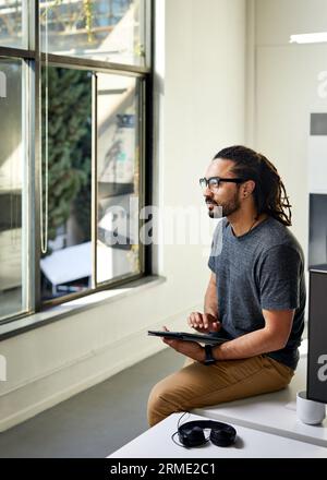 Seitenansicht eines nachdenklichen Geschäftsmannes mit Tablet-Computer, der auf dem Schreibtisch im Büro sitzt Stockfoto