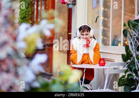 Glückliche junge Frau in Paris an einem Wintertag, trinken Kaffee, Tee oder heiße Schokolade in Pariser Outdoor-Café dekoriert zu Weihnachten Stockfoto