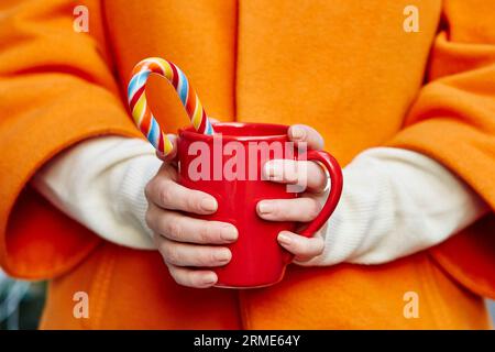 Die Frau hält Wollhandschuhe in einer gemütlichen Tasse mit heißem Kakao, Tee oder Kaffee und einem Zuckerrohr Stockfoto