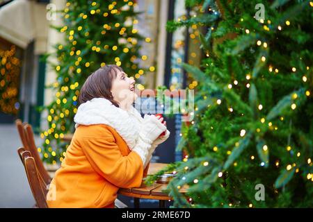 Glückliche junge Frau in Paris an einem Wintertag, trinken Kaffee, Tee oder heiße Schokolade in Pariser Outdoor-Café dekoriert zu Weihnachten Stockfoto