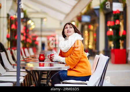 Glückliche junge Frau in Paris an einem Wintertag, trinken Kaffee, Tee oder heiße Schokolade in Pariser Outdoor-Café dekoriert zu Weihnachten Stockfoto