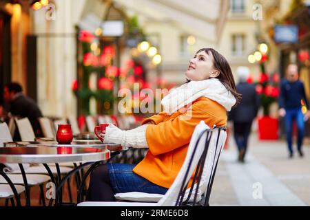 Glückliche junge Frau in Paris an einem Wintertag, trinken Kaffee, Tee oder heiße Schokolade in Pariser Outdoor-Café dekoriert zu Weihnachten Stockfoto