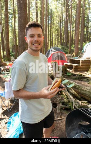 Mann genießt Hot Dog beim Grillen auf dem Campingplatz BBQ Stockfoto