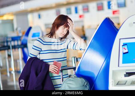 Junge weibliche Passagierin am Flughafen, die sich selbst eincheckt, gestresst und besorgt. Konzept für verpasste, verspätete oder stornierte Flüge Stockfoto