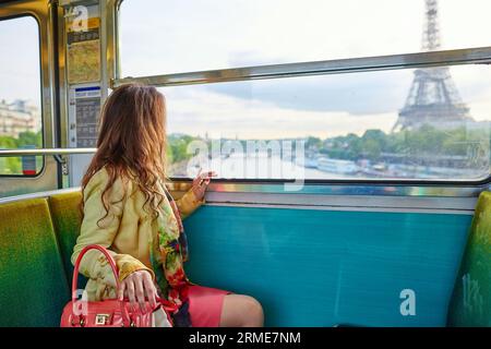 Wunderschöne junge Frau, die in einem Zug aus der Pariser U-Bahn reist und durch das Fenster auf den Eiffelturm blickt Stockfoto