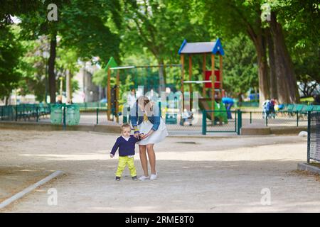 Die schöne junge Mutter und ihr entzückender Kleinkind-Sohn haben Spaß zusammen auf einem Pariser Spielplatz, Junge küsst seine Mami Stockfoto