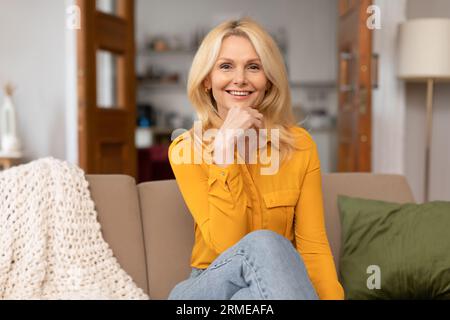 Porträt einer blonden Frau mittleren Alters, die auf dem Sofa sitzt Stockfoto