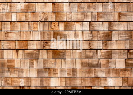 Schindelrotes Zedernholz Shake Holz Seitenreihen Dachplatte aus Lärchenkonifer Baum. Hintergrund aus Holzschindeln. Braune Holzschindeln Hintergrundstruktur. Hauswand mit Holzfliesen als Hintergrund Stockfoto