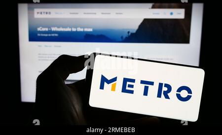 Person mit Smartphone mit Logo des deutschen Großhandelsunternehmens Metro AG auf dem Bildschirm vor der Website. Konzentrieren Sie sich auf das Display des Telefons. Stockfoto