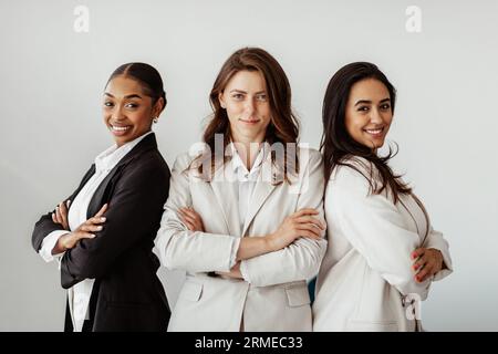 Drei erfolgreiche multikulturelle Geschäftsfrauen stehen mit gekreuzten Armen und lächeln vor der Kamera, posieren im Büro Stockfoto