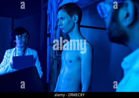 Futuristisches Konzept, unbekannte kosmische Kreatur in der Nähe von Wissenschaftlern in Neon-beleuchtetem Innovationszentrum Stockfoto