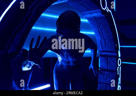 Kosmisches Phänomen, extraterrestrisches Humanoid in der Nähe von experimentellen Geräten im neonbeleuchteten Wissenschaftszentrum Stockfoto