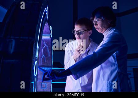 innovation hub, woman scientist operating new equipment near young intern in science center Stockfoto