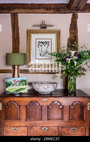 Moderne Kunst mit Blumen auf antikem Sideboard im Tudor Farmhaus mit Fachwerkrahmen, Surrey, Großbritannien Stockfoto