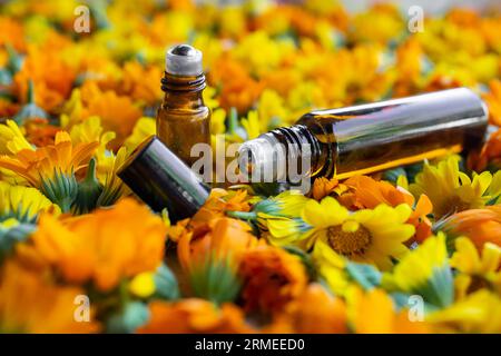 Rollen Sie Flaschen mit ätherischem Öl auf das Ringelblumenbett, weicher Fokus aus nächster Nähe. Stockfoto