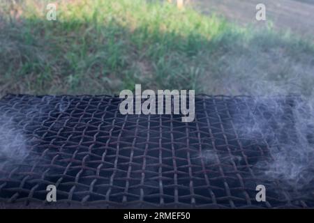 Leerer Metallgitter mit Rauch und Gras im Hintergrund, weicher Fokus Nahaufnahme Stockfoto