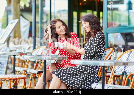 Wunderschöne Zwillingsschwestern trinken Kaffee in einem gemütlichen Café im Freien in Paris, Frankreich. Glückliche lächelnde Mädchen genießen ihren Urlaub in Europa Stockfoto