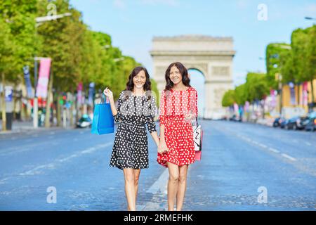 Glückliche Zwillingsschwestern, die während ihres Urlaubs in Frankreich shoppen gehen, mit Einkaufstaschen vor dem Arc de Triomphe auf der Champs-Elysees, Paris, Frankreich Stockfoto