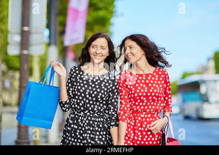 Glückliche Zwillingsschwestern, die während ihres Urlaubs in Frankreich shoppen gehen, mit Einkaufstaschen vor dem Arc de Triomphe auf der Champs-Elysees, Paris, Frankreich Stockfoto