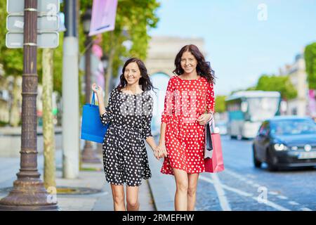 Glückliche Zwillingsschwestern, die während ihres Urlaubs in Frankreich shoppen gehen, mit Einkaufstaschen vor dem Arc de Triomphe auf der Champs-Elysees, Paris, Frankreich Stockfoto