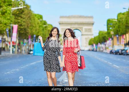 Glückliche Zwillingsschwestern, die während ihres Urlaubs in Frankreich shoppen gehen, mit Einkaufstaschen vor dem Arc de Triomphe auf der Champs-Elysees, Paris, Frankreich Stockfoto