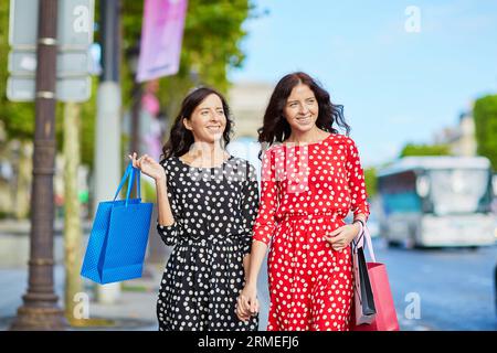 Glückliche Zwillingsschwestern, die während ihres Urlaubs in Frankreich shoppen gehen, mit Einkaufstaschen vor dem Arc de Triomphe auf der Champs-Elysees, Paris, Frankreich Stockfoto