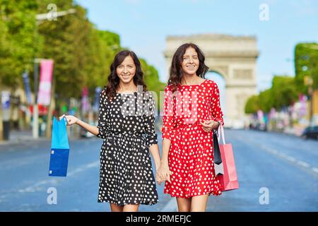 Glückliche Zwillingsschwestern, die während ihres Urlaubs in Frankreich shoppen gehen, mit Einkaufstaschen vor dem Arc de Triomphe auf der Champs-Elysees, Paris, Frankreich Stockfoto