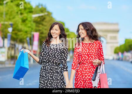 Glückliche Zwillingsschwestern, die während ihres Urlaubs in Frankreich shoppen gehen, mit Einkaufstaschen vor dem Arc de Triomphe auf der Champs-Elysees, Paris, Frankreich Stockfoto