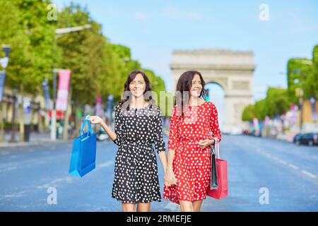 Glückliche Zwillingsschwestern, die während ihres Urlaubs in Frankreich shoppen gehen, mit Einkaufstaschen vor dem Arc de Triomphe auf der Champs-Elysees, Paris, Frankreich Stockfoto