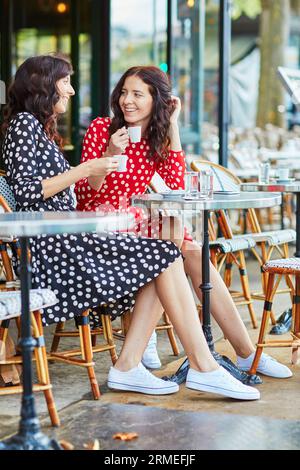 Wunderschöne Zwillingsschwestern trinken Kaffee in einem gemütlichen Café im Freien in Paris, Frankreich. Glückliche lächelnde Mädchen genießen ihren Urlaub in Europa Stockfoto