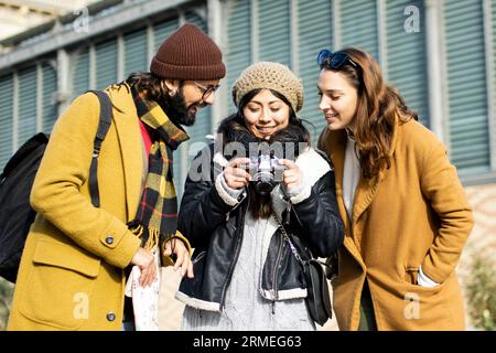 Eine Gruppe von Touristen, die auf der Straße eine Kamera suchen. Drei fröhliche Freunde machen ein Foto während einer Städtereise Stockfoto