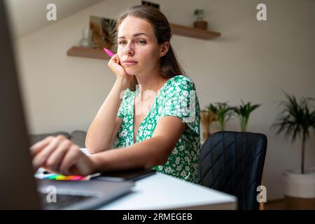 Erwachsene, brünette Frau, die am Schreibtisch sitzt und ihren Laptop benutzt, Erwachsene Studentin, die sich Online-Lehrvideos ansieht. Stockfoto