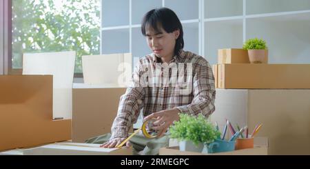 Young asian man smiling confident unpacking cardboard box at new home Stockfoto