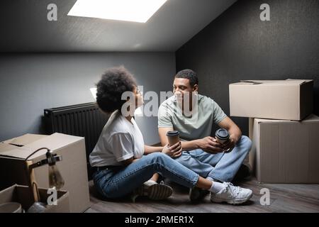 afroamerikanische Frau mit Kaffee zum Mitnehmen mit Freund in der Nähe von Kästen auf dem Dachboden in einem neuen Haus Stockfoto