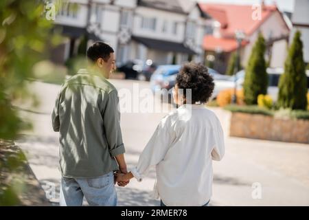 Seitenansicht des fröhlichen afroamerikanischen Paares, das sich mit den Händen redet und auf der Straße spaziert Stockfoto