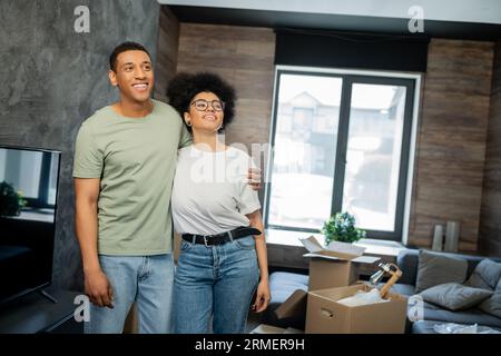 Traumhaftes und lächelndes afroamerikanisches Paar, das sich in der Nähe von caron-Boxen in einem neuen Haus umarmt Stockfoto