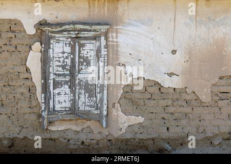 Alte lehmziegelmauer mit alten schäbigen geschlossenen Holzfenstern und abblättertem Putz Stockfoto