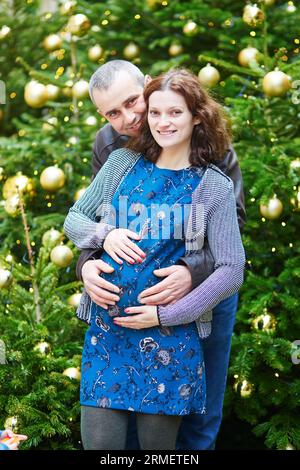 Wunderschönes erwartendes Paar, Ehemann und seine schwangere Frau, in der Nähe des geschmückten Weihnachtsbaums Stockfoto