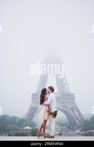 Wunderschönes, romantisches Paar, das sich in der Nähe des Eiffelturms in Paris an einem bewölkten und nebelverregneten Tag verliebt hat Stockfoto