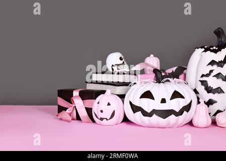 Rosafarbene und weiße Halloween-Einrichtung mit schwarz-weißen Kürbissen, Geschenkboxen und Zauberbüchern auf grauem Hintergrund Stockfoto