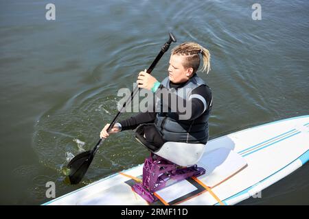 Hochwinkelporträt eines Jungen mit Behinderung, der mit adaptiver Sportausrüstung SUP-Boarding auf dem Wasser genießt Stockfoto