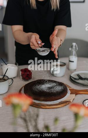 Frau, die Puderzucker auf frisch gebackenen Schokoladenkuchen aufträgt Stockfoto