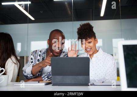 Lächelnde Kollegen, die bei Geschäftstreffen sitzen und ein digitales Tablet verwenden Stockfoto