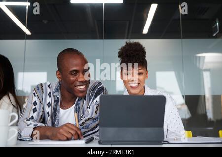 Lächelnde Kollegen, die bei Geschäftstreffen sitzen und ein digitales Tablet verwenden Stockfoto