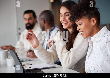 Lächelnde Frauen sitzen auf einem Geschäftstreffen und schauen sich einen Laptop an Stockfoto