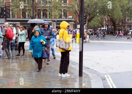 Menschen Fußgänger, die in der Straße gehen Frau trägt Regenmäntel Regenmantel an einem nassen regnerischen Sommertag August wartet an der Verkehrsampel London KATHY DEWITT Stockfoto