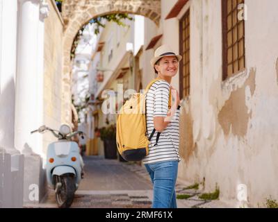 Sommerausflug zur Insel Rhodos, Griechenland. Junge Asiatin in gestreiftem T-Shirt und Hut wandelt in der Straße der Ritterburg. Weibliche Reisende Stockfoto