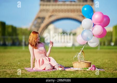 Schöne junge Frau in rosa Kleid mit Ballons beim Picknick in der Nähe des Eiffelturms in Paris, Frankreich Stockfoto